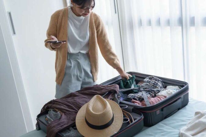 Une femme vérifie sa liste de voyage sur son smartphone en remplissant sa valise.