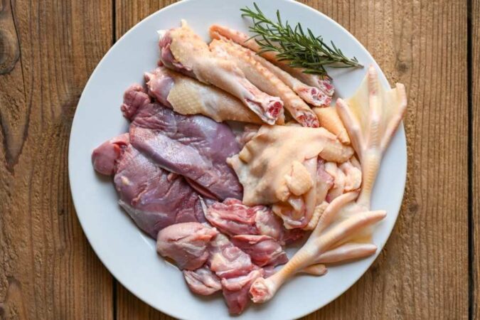 Assortiment de morceaux de canard crus sur une assiette blanche avant la cuisson d'un magret au barbecue.