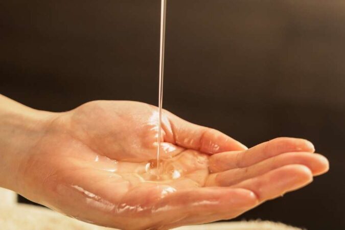 De l'huile de massage fluide coule en filet directement dans le creux d'une main ouverte.
