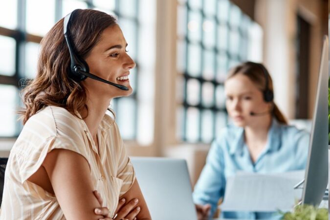 Une conseillère souriante avec un micro-casque discute avec un client dans un bureau lumineux.
